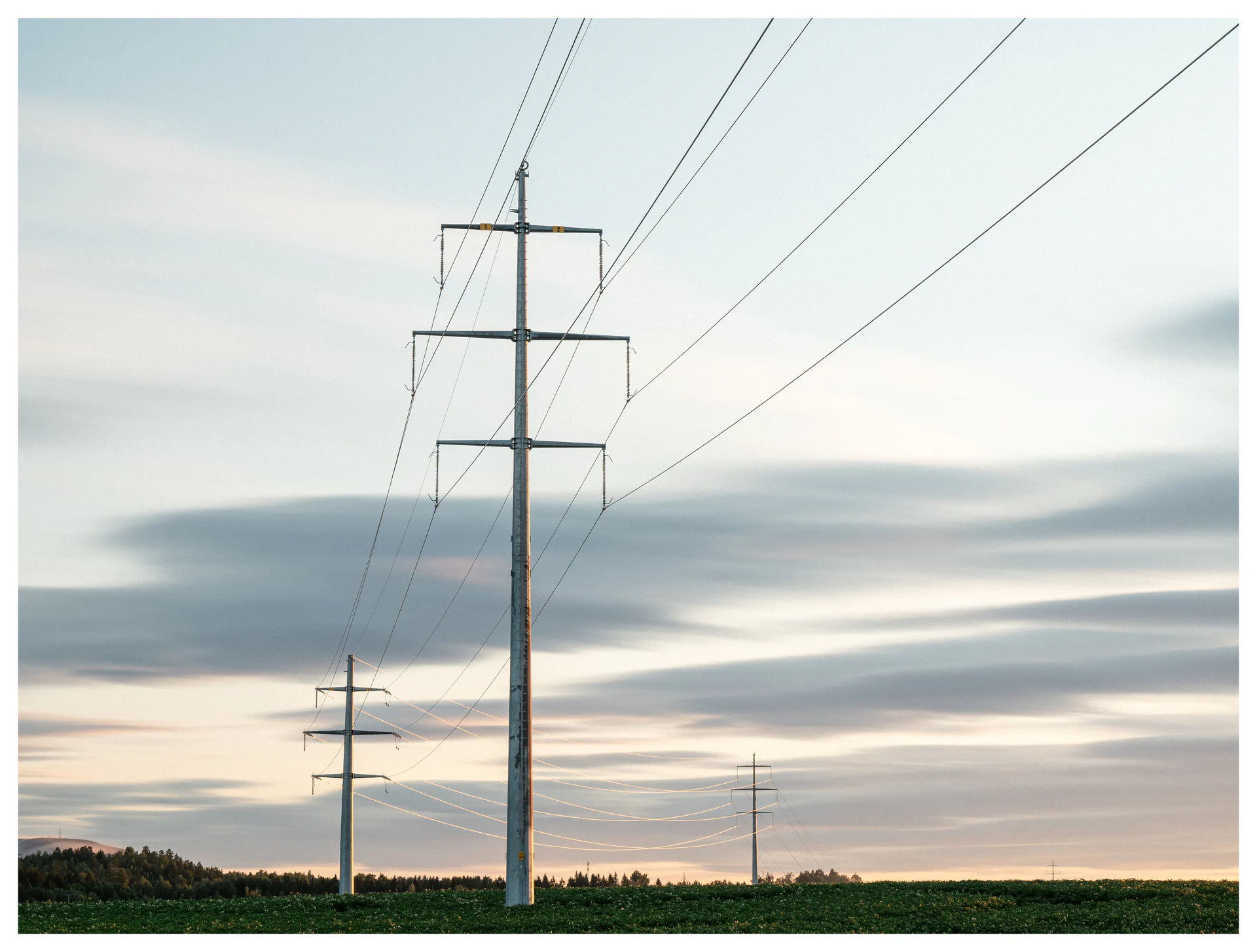 High-voltage power lines crossing open fields beneath layered clouds.