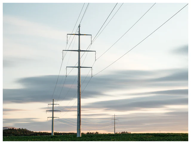 High-voltage power lines crossing open fields beneath layered clouds.