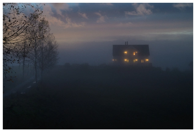 A misty rural evening with a solitary house glowing warmly through the fog, evoking a feeling of homecoming and longing.