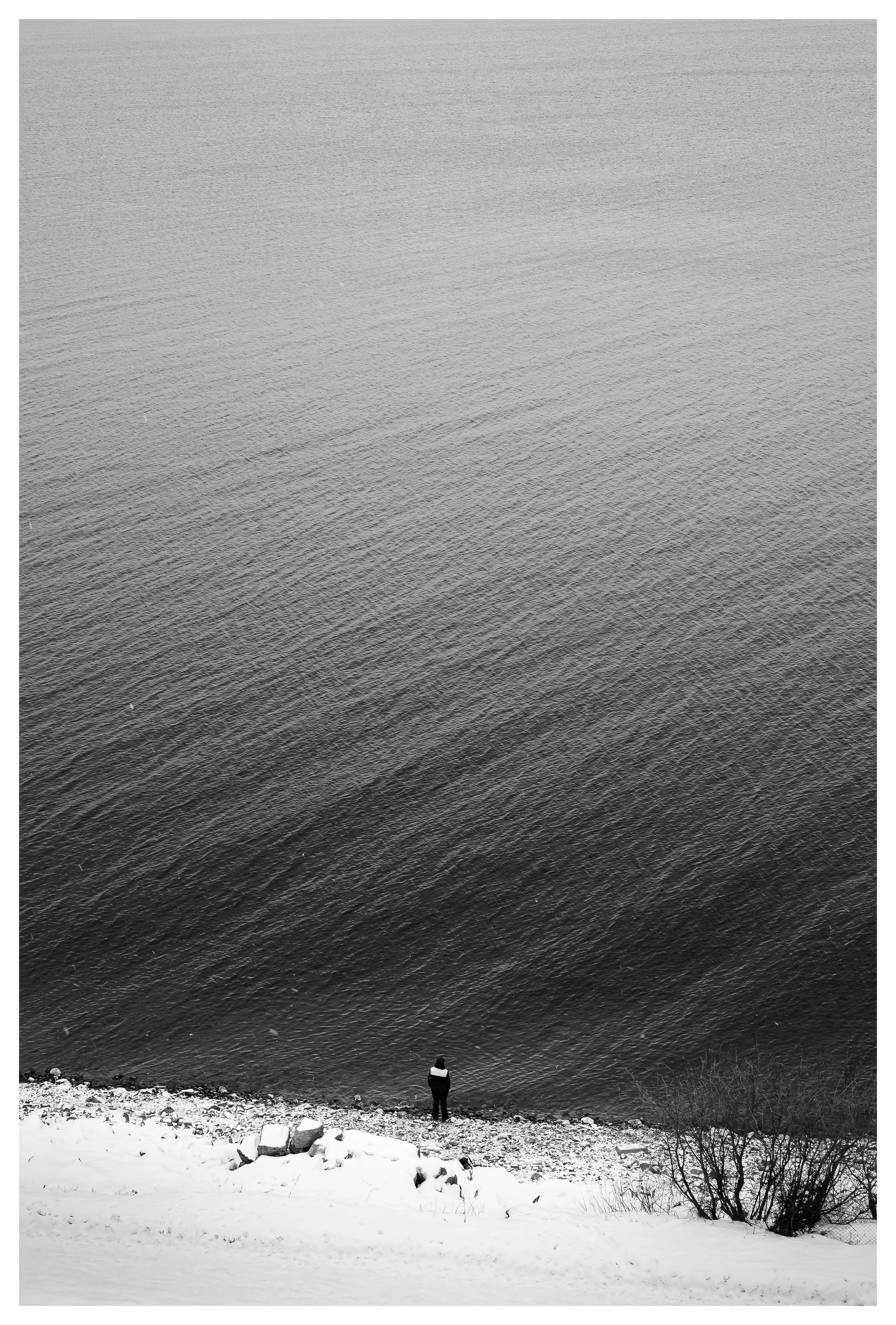 A solitary person standing by the edge of a lake in winter, surrounded by still water and snow.
