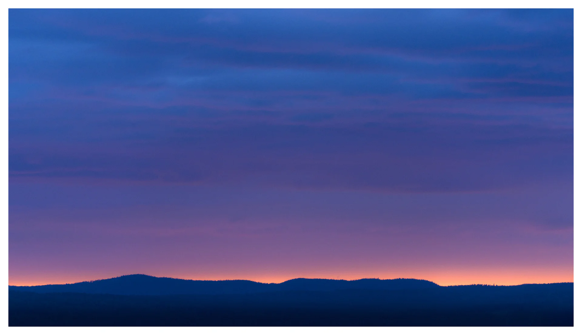 Minimalist landscape at dusk with a dark distant ridge beneath a vast blue and violet sky, with a narrow band of warm light along the horizon.