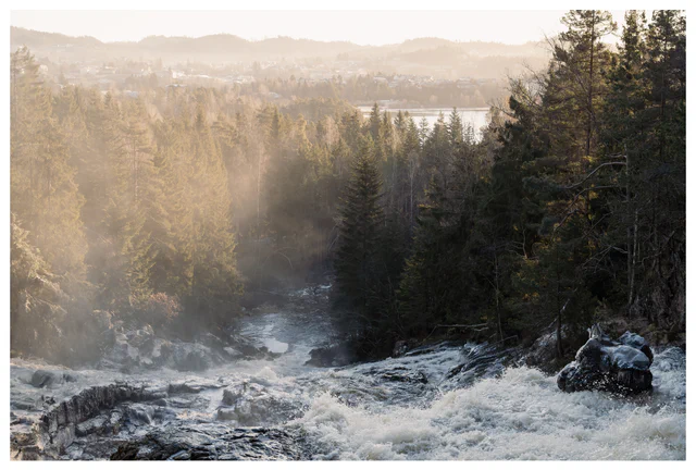 River rushing through a forested valley with soft morning mist and distant hills fading into light.