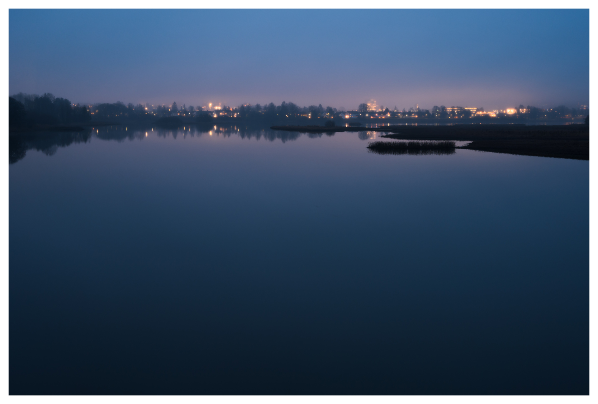 Still water reflecting the distant lights of Lillestrøm, photographed from Nebbursvollen at night.