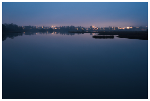 Still water reflecting the distant lights of Lillestrøm, photographed from Nebbursvollen at night.