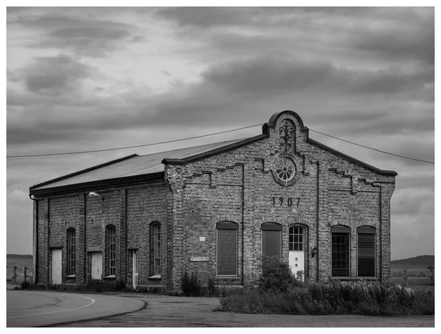 Historic brick industrial building from 1907 under a cloudy sky in rural Norway, photographed in black and white.