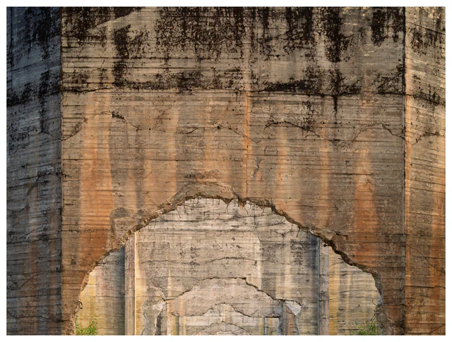 Repeating damaged concrete arches recede into the distance, their weathered surfaces marked by cracks, stains and exposed reinforcement.