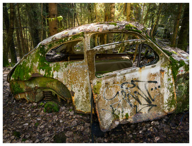 Abandoned vintage car covered in moss and graffiti in forest at Båstnäs Car Graveyard Sweden