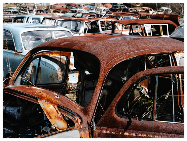 Cluster of rusting vintage cars at Båstnäs Car Graveyard in Sweden with rows of abandoned vehicles in open scrapyard