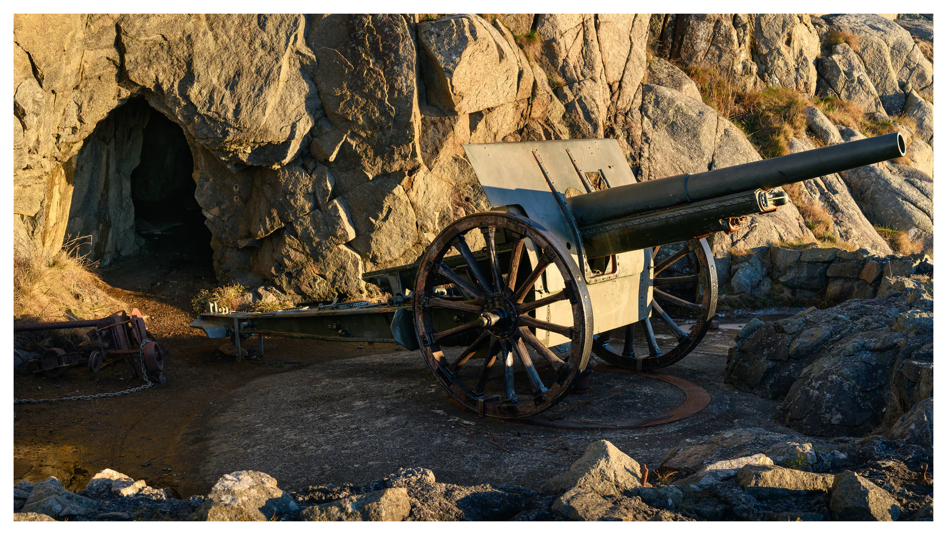 Old coastal artillery cannon positioned beside a rock tunnel at Hausvikodden Fort, lit by low winter sun and looking out toward the coastline.
