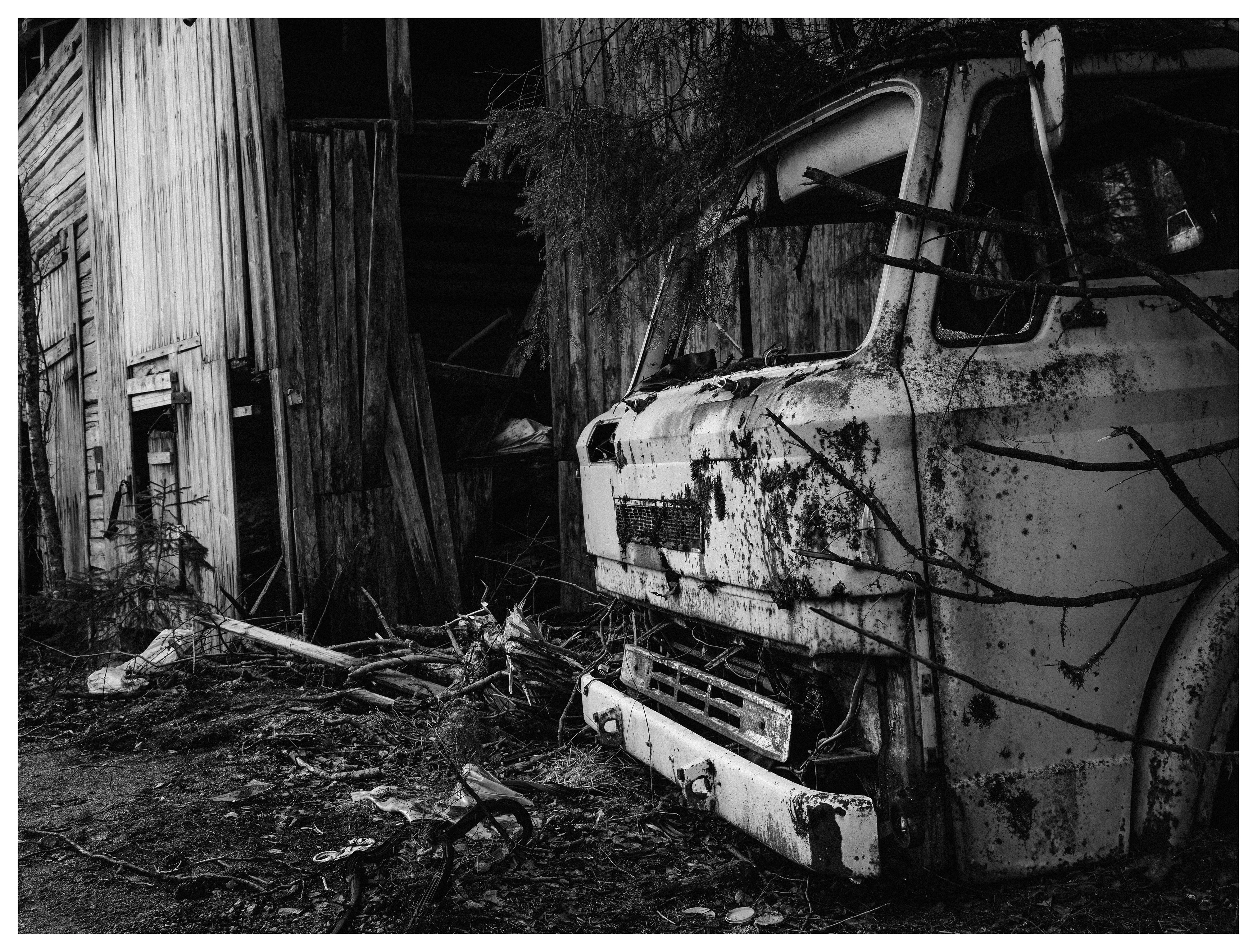 Abandoned truck beside collapsing wooden barn in black and white rural landscape.