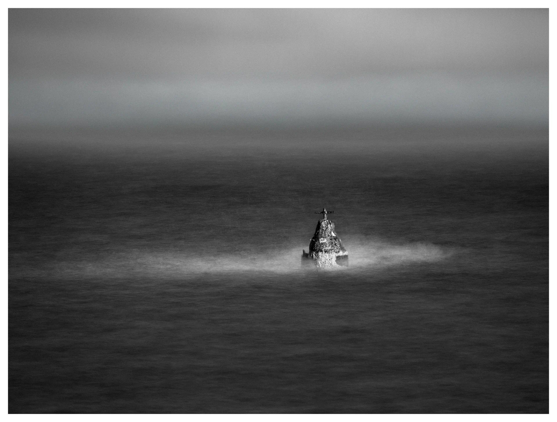 Solitary navigation marker surrounded by misty water on a dark lake under an overcast sky.