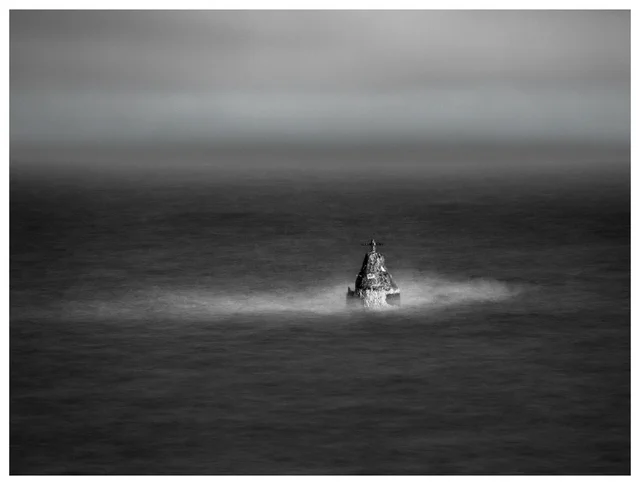 Solitary navigation marker surrounded by misty water on a dark lake under an overcast sky.