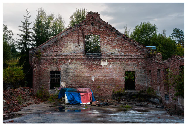 Front view of a roofless brick hall at the abandoned Mago C power plant in Eidsvoll, with broken windows, exposed walls, scattered debris, and a colorful tarp on the ground.