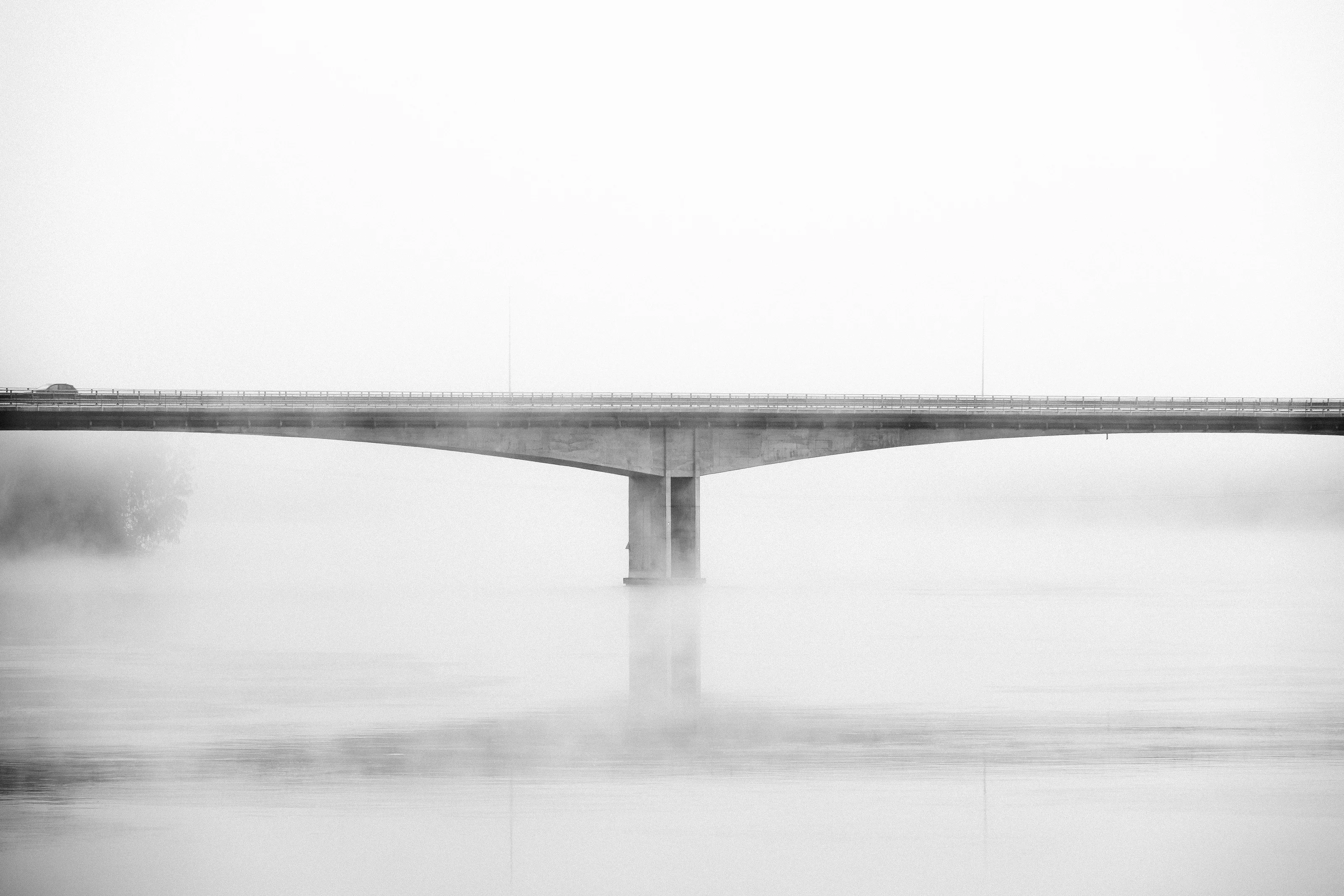 Bridge crossing calm water in morning fog in Norway.