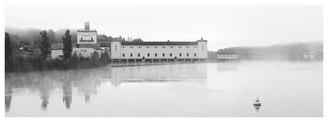 Rånåsfoss II Power Station reflected in calm water as morning fog drifts across the river, with a small buoy in the foreground.
